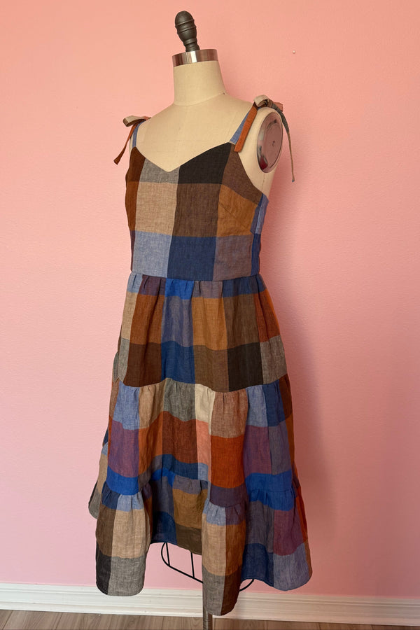 Custom made tiered cami dress with tie straps and  gathered tiered skirt in a large scale checker pattern in shades of brown, gray, and blue. Shown on a mannequin with a pink background.
